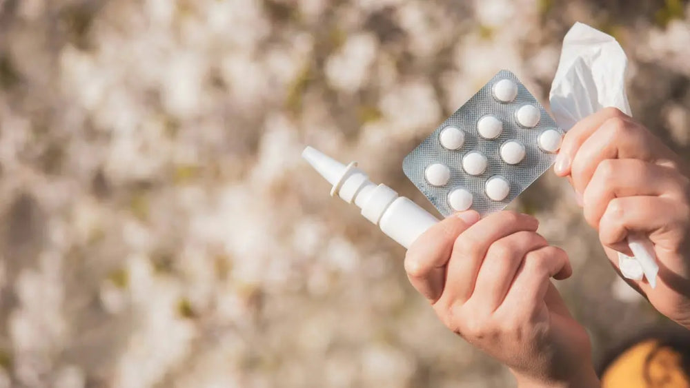 hands holding up a blister pack of tablets, nasal spray,  and tissues