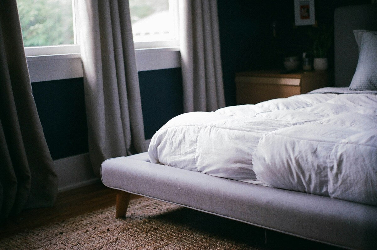 Outer corner of bed in bedroom stripped bare, except for mattress topper 